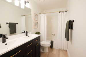 Full bath featuring double vanity, shower / bathtub combination with curtain, and light wood-style floors