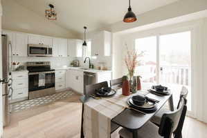 Kitchen featuring stainless steel appliances, vaulted ceiling, light countertops, white cabinets, and light wood-style flooring