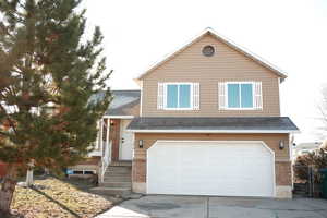 View of front facade with an attached garage, driveway, a gate, roof with shingles, and brick siding