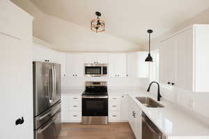 Kitchen with stainless steel appliances, pendant lighting, white cabinetry, lofted ceiling, and light wood-style flooring