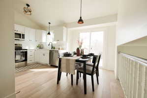 Kitchen with stainless steel appliances, light countertops, white cabinetry, vaulted ceiling, and light wood finished floors