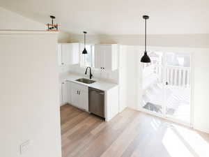 Bar featuring white cabinetry, light countertops, decorative light fixtures, light wood finished floors, and dishwasher