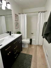 Bathroom with double vanity, shower / tub combo with curtain, and light wood-style flooring