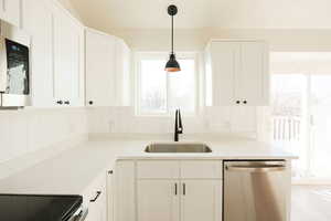 Kitchen with stainless steel appliances, white cabinetry, light stone counters, and pendant lighting