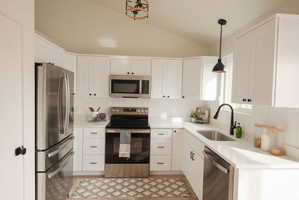 Kitchen featuring stainless steel appliances, white cabinets, lofted ceiling, decorative backsplash, and decorative light fixtures