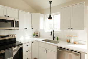 Kitchen featuring stainless steel appliances, white cabinetry, pendant lighting, vaulted ceiling, and light stone counters