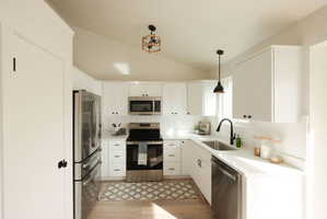 Kitchen featuring stainless steel appliances, white cabinetry, decorative backsplash, pendant lighting, and vaulted ceiling