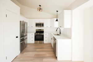 Kitchen with stainless steel appliances, decorative light fixtures, vaulted ceiling, white cabinets, and light stone countertops