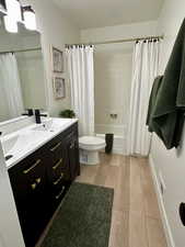 Full bath featuring double vanity, shower / tub combo with curtain, and light wood finished floors