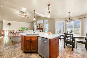 Kitchen featuring a kitchen island with sink, stainless steel dishwasher, hanging light fixtures, wood finish cabinetry, and vaulted ceiling