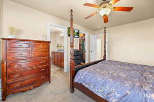 Bedroom with light colored carpet, a ceiling fan, a walk in closet, and connected bathroom