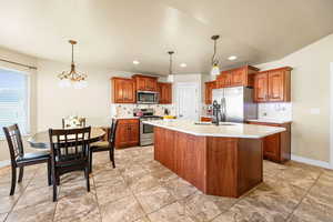 Kitchen with wood finish cabinetry, stainless steel appliances, an island with sink, hanging lights, and backsplash