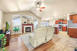 Living room featuring a fireplace, light wood finished floors, ceiling fan, and a high ceiling