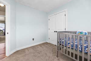 Bedroom featuring light colored carpet, a crib, and a closet