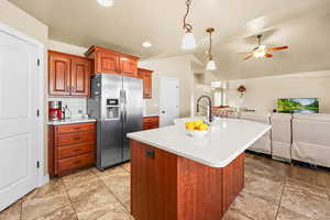 Kitchen featuring decorative light fixtures, stainless steel fridge with ice dispenser, wood finish cabinets, tasteful backsplash, and vaulted ceiling