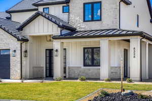 Doorway to property with stone siding, board and batten siding, a porch, a lawn, and a standing seam roof