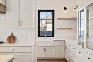 Kitchen featuring white cabinets, open shelves, wood finished floors, and light stone counters