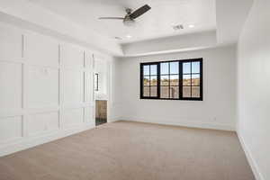 Unfurnished bedroom with a raised ceiling, light colored carpet, a decorative wall, ensuite bathroom, and ceiling fan