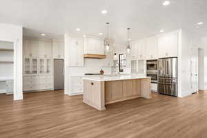 Dual tone kitchen featuring stainless steel appliances, two tone color scheme, pendant lighting, light wood-style flooring, and a center island with sink