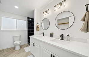 Master bathroom featuring double vanity, a tile shower, light wood-style floors, and recessed lighting