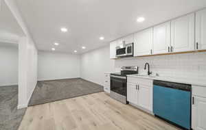 Kitchen with stainless steel appliances, light wood-style flooring, white cabinets, recessed lighting, and tasteful backsplash