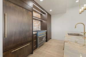 Kitchen with light stone countertops, high end stainless steel range, light wood-style floors, pendant lighting, and open shelves