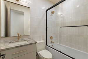 Ensuite bathroom  for bedroom 4 with bath / shower combo with glass door, vanity, and tile walls