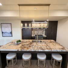 Kitchen with a kitchen bar, dark wood finish cabinets, a large island with sink, and decorative light fixtures