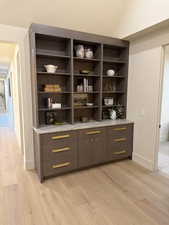 Bar area with modern cabinets, light wood-style flooring, light stone countertops, lofted ceiling, and dark wood finish cabinets