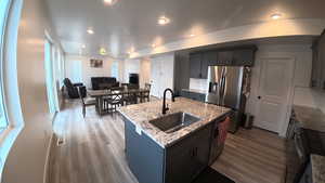 Kitchen with stainless steel appliances, a kitchen island with sink, light stone countertops, light wood finished floors, and open floor plan