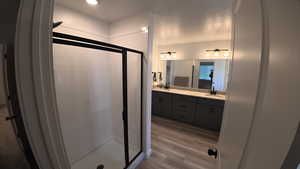 Bathroom with light wood-type flooring, double vanity, a shower stall, and recessed lighting