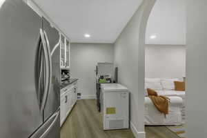Kitchen featuring freestanding refrigerator, glass insert cabinets, white cabinets, arched walkways, and light wood finished floors