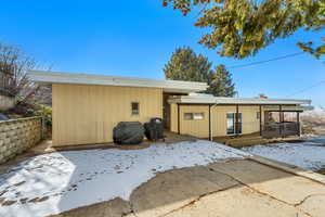 Snow covered back of property with a patio