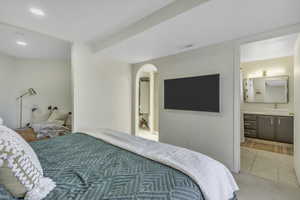 Bedroom featuring ensuite bathroom, tile patterned flooring, recessed lighting, and arched walkways