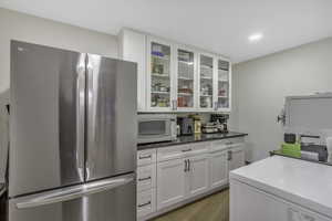 Kitchen featuring freestanding refrigerator, white cabinetry, white microwave, glass insert cabinets, and light wood-type flooring