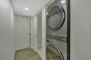 Washroom with light wood-type flooring, estacked washer and dryer, and recessed lighting