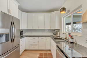 Kitchen featuring appliances with stainless steel finishes, dark stone countertops, light wood-style flooring, and white cabinets
