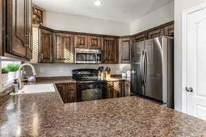Kitchen featuring dark wood finish cabinetry, stainless steel appliances, dark stone counters, a peninsula, and recessed lighting