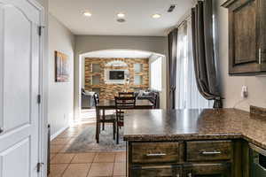 Kitchen featuring dark wood finish cabinets, a peninsula, light tile patterned floors, open floor plan, and recessed lighting