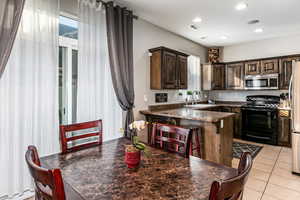 Kitchen with dark wood finish cabinets, stainless steel appliances, a breakfast bar, light tile patterned flooring, and a peninsula