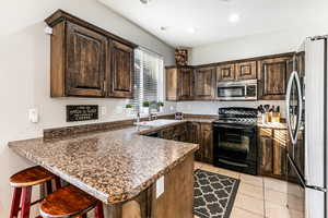 Kitchen with dark wood finish cabinets, stainless steel appliances, a peninsula, a breakfast bar, and light tile patterned floors