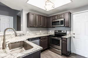 Kitchen featuring stainless steel appliances, dark wood finish cabinets, light wood-style flooring, and light stone countertops