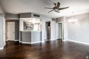 Unfurnished living room featuring a chandelier, a ceiling fan, and dark wood-style floors
