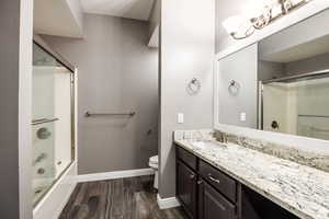 Bathroom with vanity, dark wood finished floors, and combined bath / shower with glass door