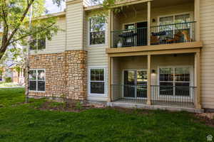 Rear view of house with stone siding, a balcony, and a yard