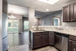 Kitchen with stainless steel appliances, light stone counters, light wood-style flooring, suspended lighting, and dark wood finish cabinets