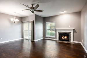 Unfurnished living room featuring a ceiling fan, a fireplace with flush hearth, suspended lighting, and dark wood-style floors