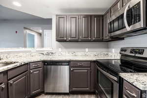 Kitchen featuring stainless steel appliances, light stone counters, recessed lighting, dark wood finish cabinetry, and light wood-style flooring