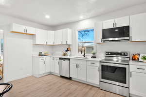 Kitchen featuring stainless steel appliances, white cabinets, light wood finished floors, recessed lighting, and light stone countertops