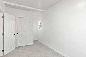 Unfurnished bedroom featuring light carpet, beam ceiling, and a textured wall
